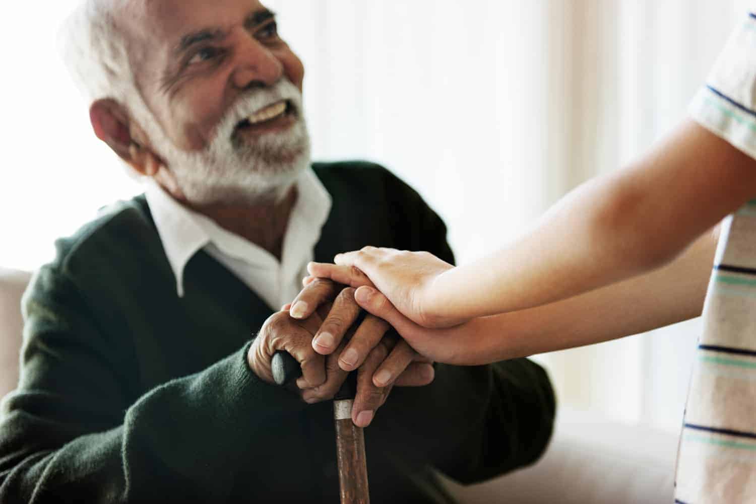 A heartwarming exchange: an elderly man with a cane smiles joyfully as he holds hands with a younger person, emphasizing a tender moment of connection and support.