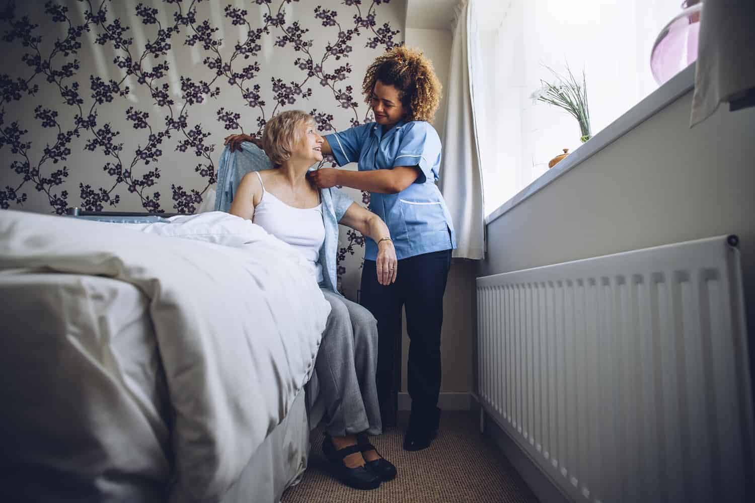 Image of a carer assisting a service user in her bedroom through our home care services .