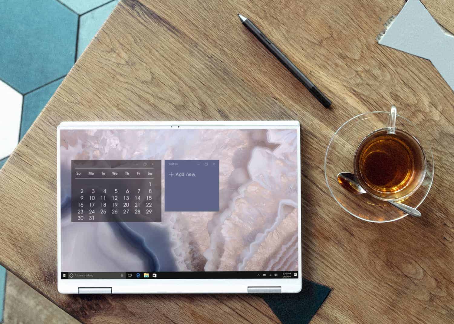 A laptop displaying a calendar application sits on a wooden table with a pen beside it, near a cup of tea with a slice of lemon, ready for a productive planning session.