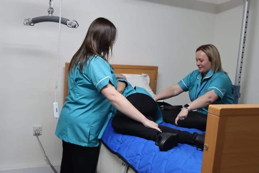 Two healthcare professionals assisting a patient in a hospital bed with mobility or physical therapy.