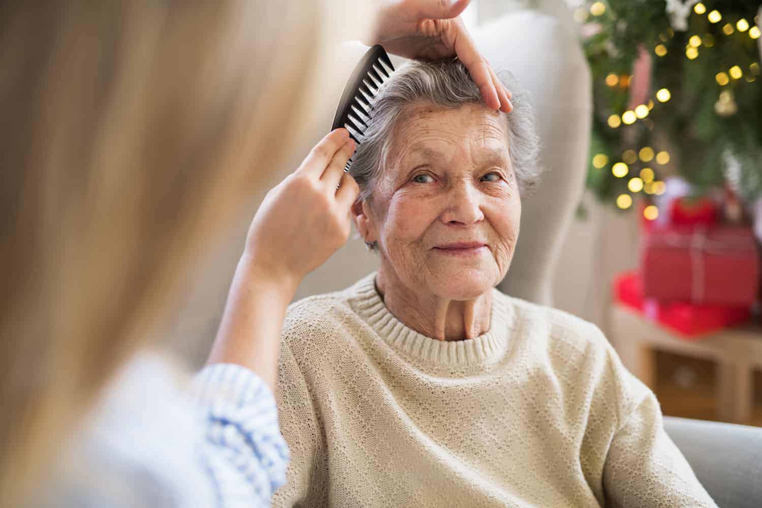 A Personal Care moment: a younger individual tenderly combs the hair of a smiling elderly woman, creating a picture of intergenerational kindness and love.