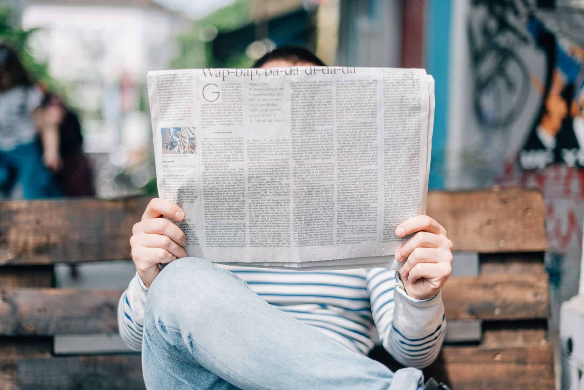 Staying informed: a person casually reads a newspaper and explores blogging tips, keeping up-to-date with world events on a relaxed day out in the city.