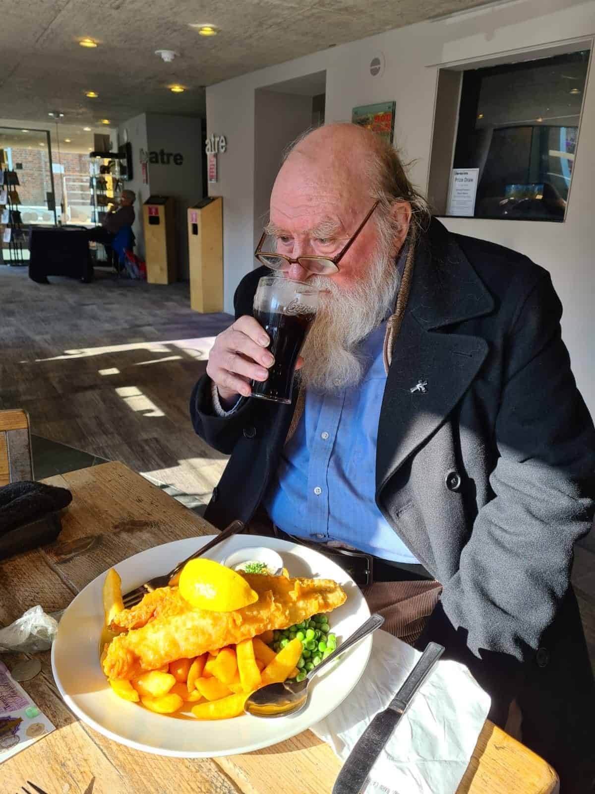 An elderly gentleman enjoying a pint and a hearty meal at a cozy restaurant.
