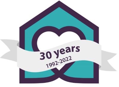 Commemorative emblem celebrating 30 years of community caring and involvement from 1992 to 2022, featuring a heart symbol inside an outline of a house with a heart, and a ribbon banner on top.