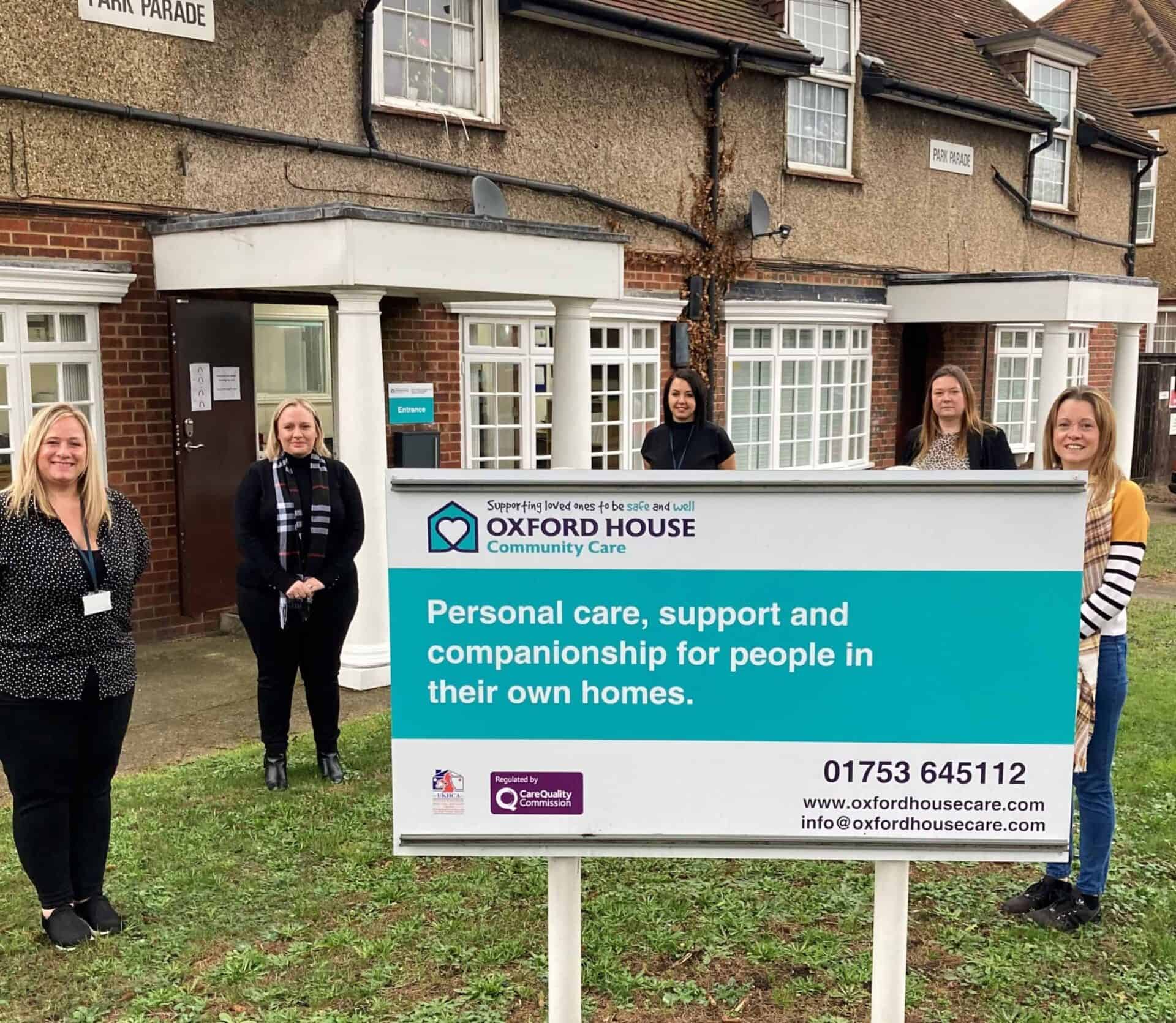 A team of professional caregivers standing proudly behind the Oxford House Community Care signage in front of the office.