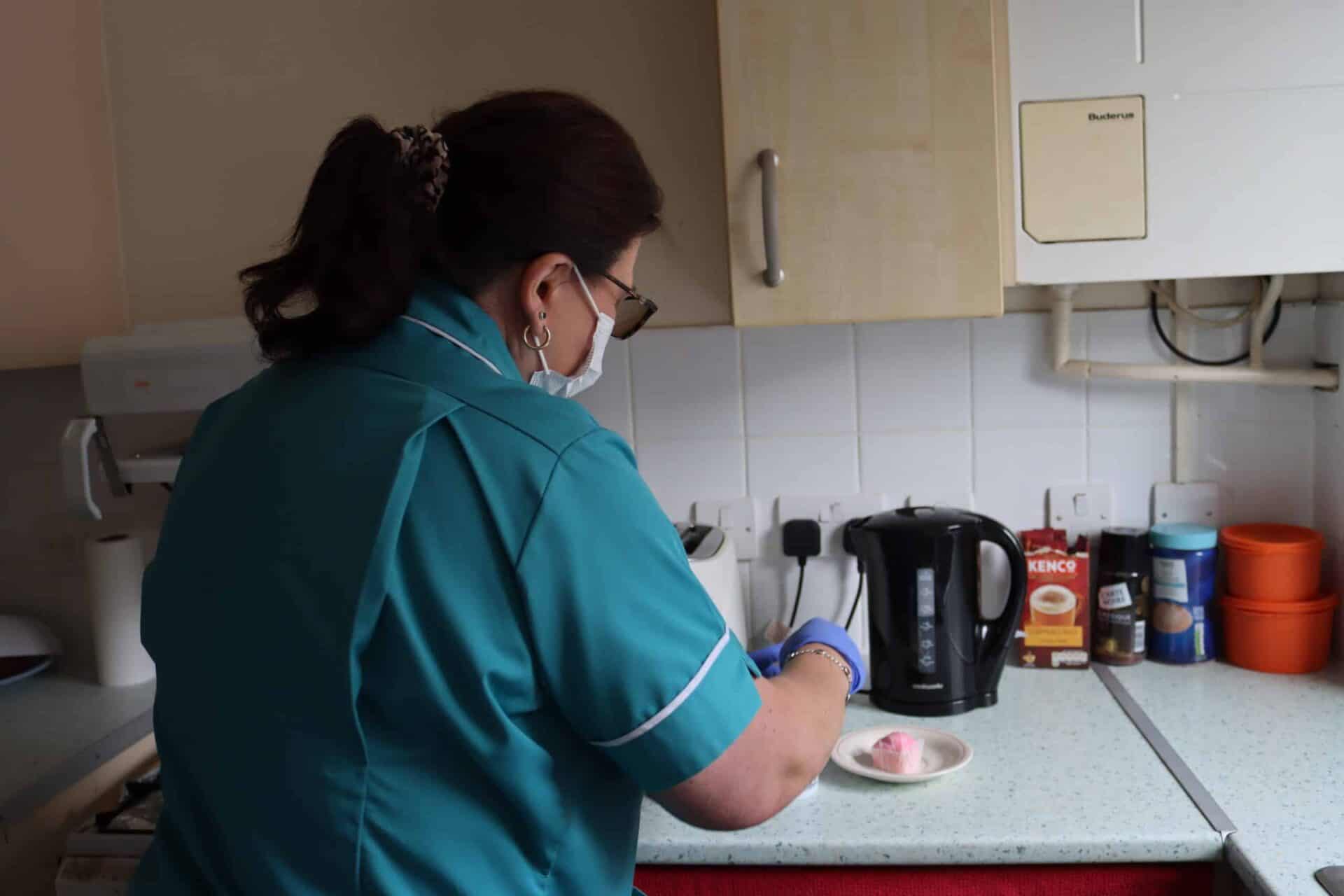 Healthcare professional in scrubs preparing a snack and beverage in a kitchen.