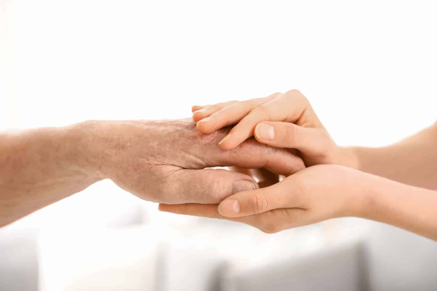A gentle younger hand holding an older one, symbolising support and compassion across generations with our home care services.