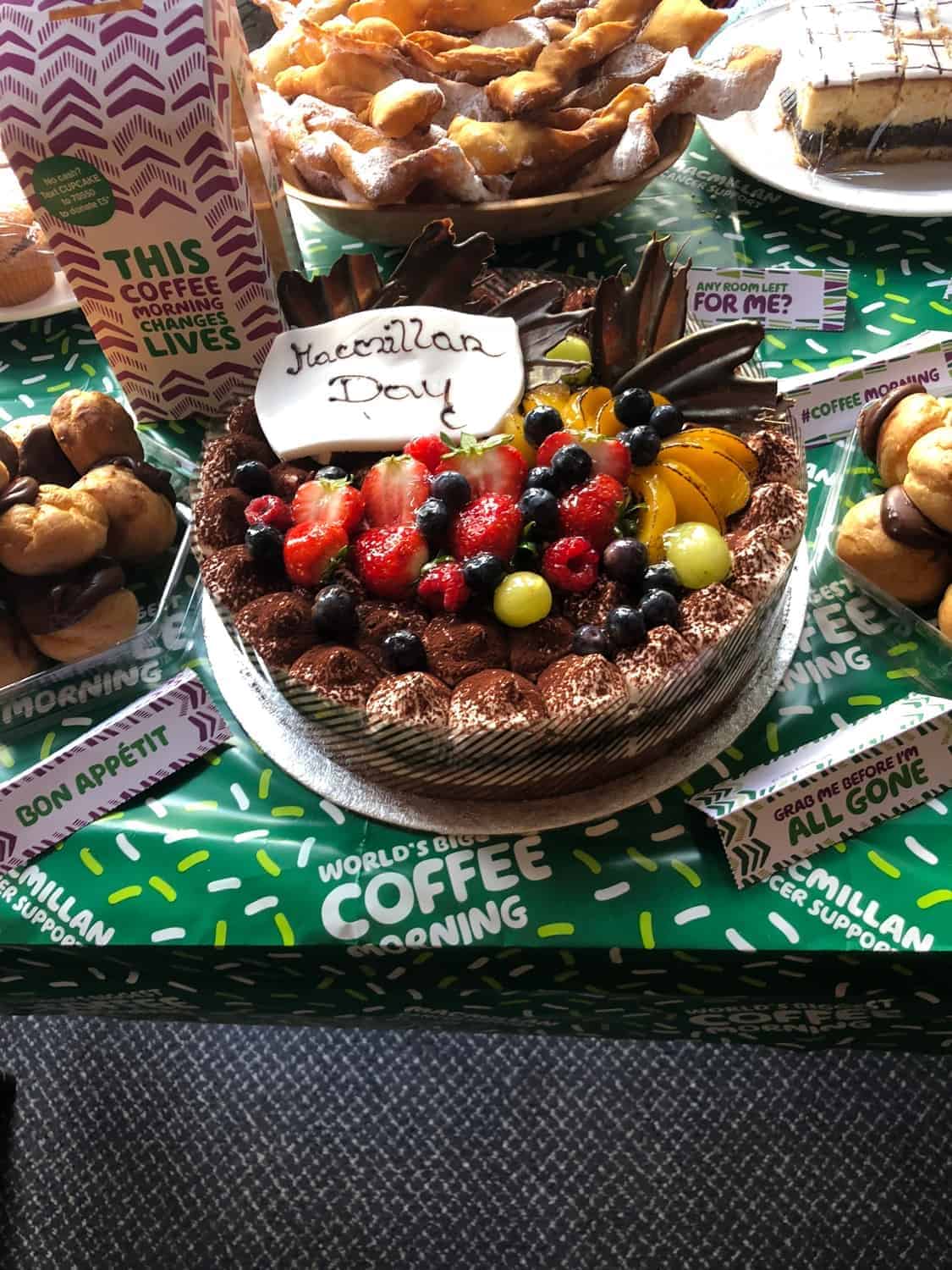 A richly garnished chocolate tart topped with an assortment of fresh strawberries, blueberries, and blackberries, with a small white plaque that reads "happy birthday," surrounded by a gallery of baked treats