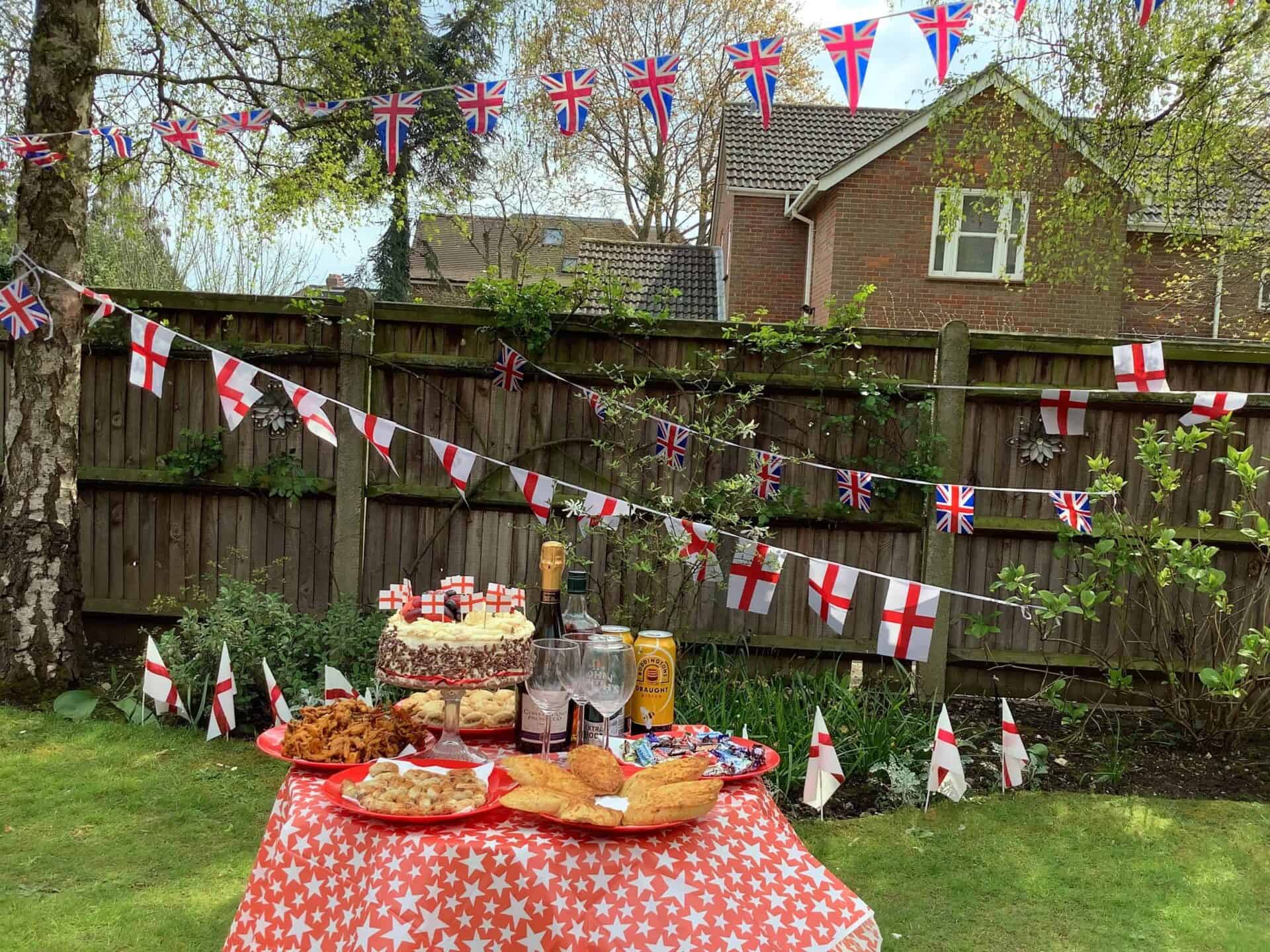 A festive garden party table laden with food under strings of British flags at Oxford House, celebrating a patriotic event outdoors.