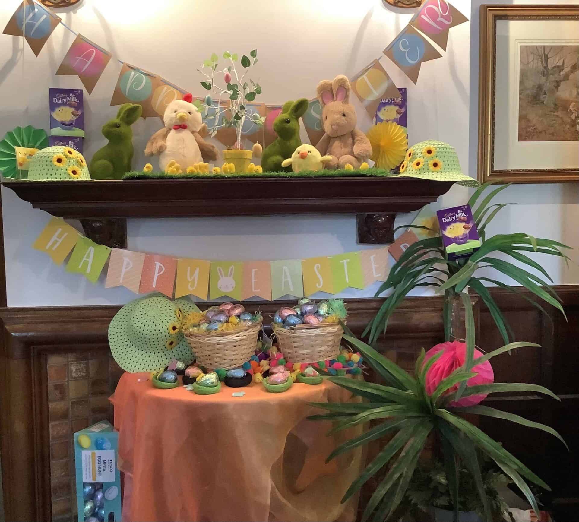 A festive Easter display with plush bunnies, colorful eggs, and themed decorations on a mantle and table at the Oxford House.