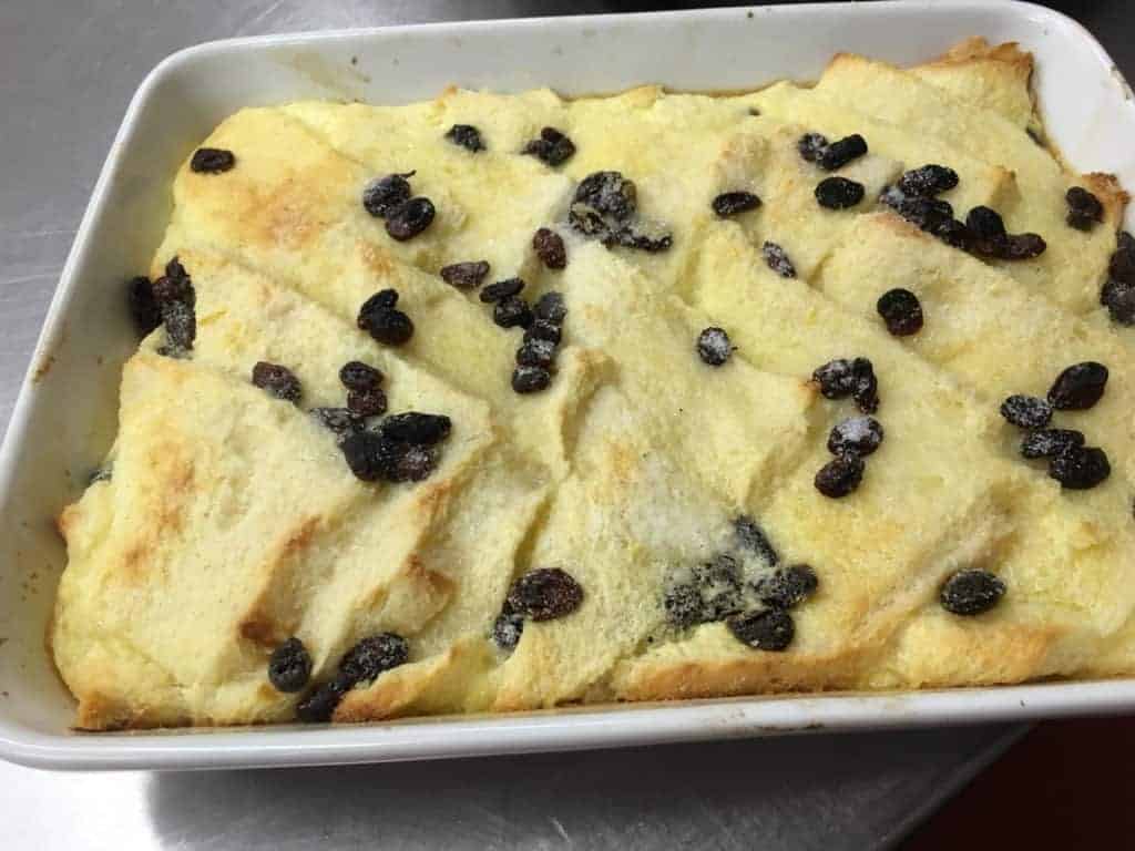 A freshly baked bread pudding sprinkled with plump raisins in a white baking dish, perfect for those who love home-cooked meals.