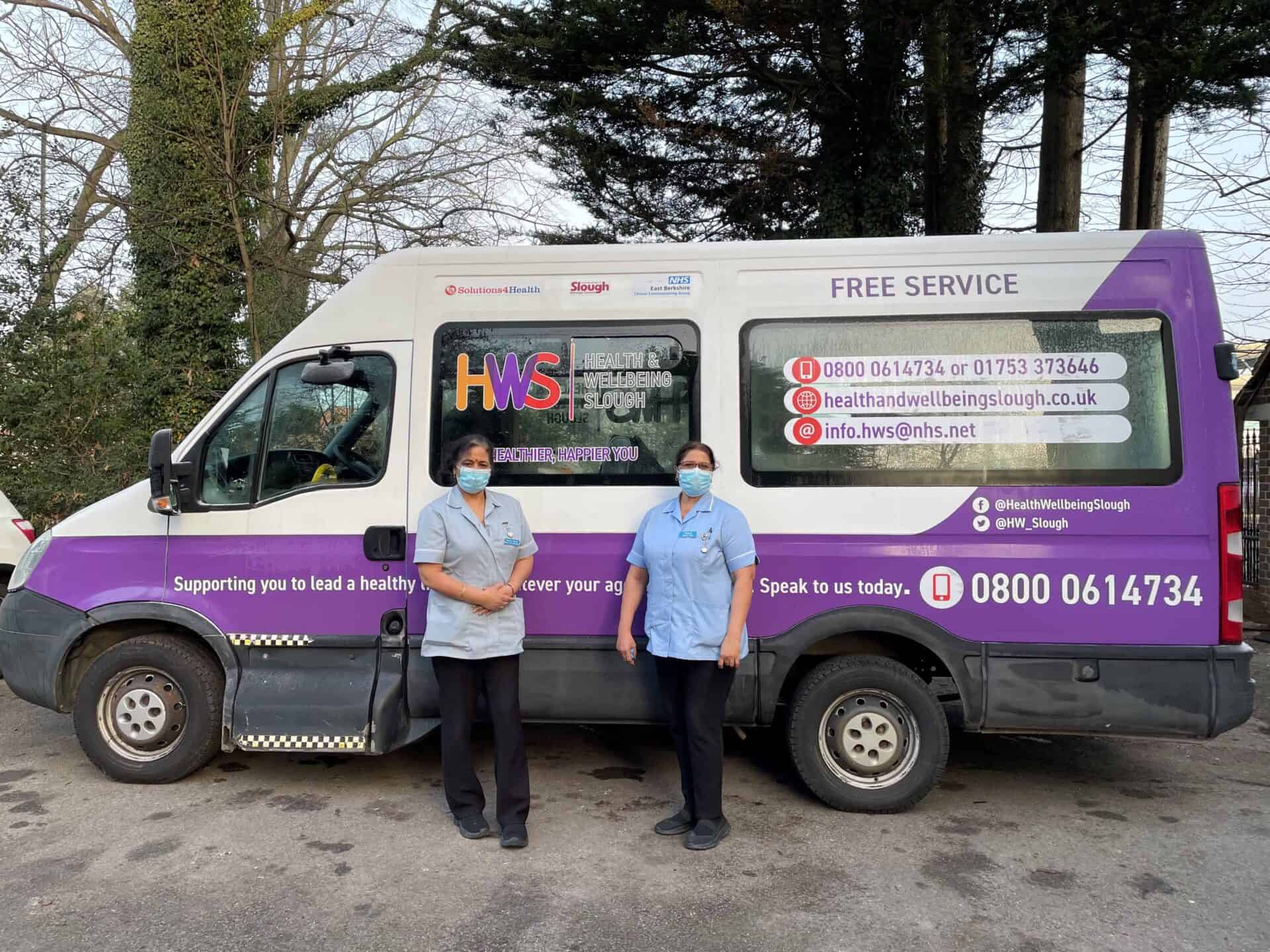 Two individuals wearing face masks and uniforms are standing in front of a Slough community health and wellbeing services van, which offers a free service, indicating a mobile healthcare initiative.