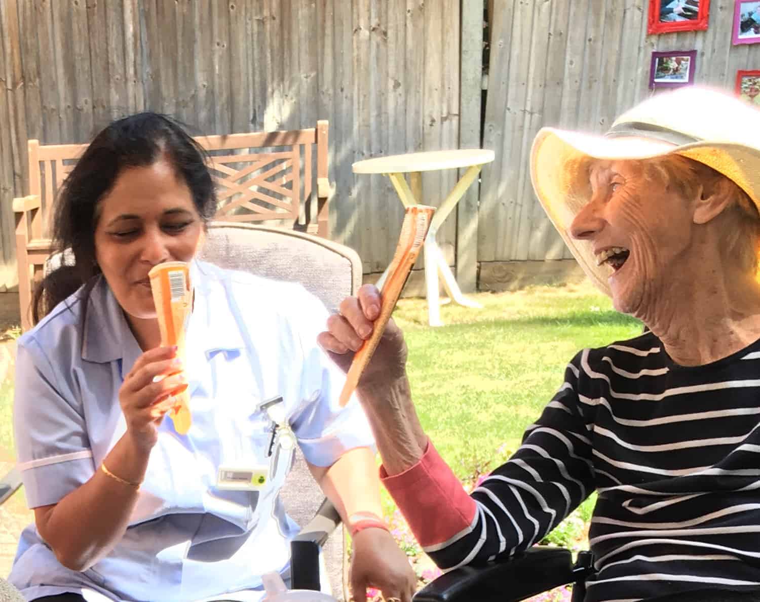 Two people enjoying a sunny day outdoors with joyful expressions, sharing a light-hearted moment over ice cream treats.