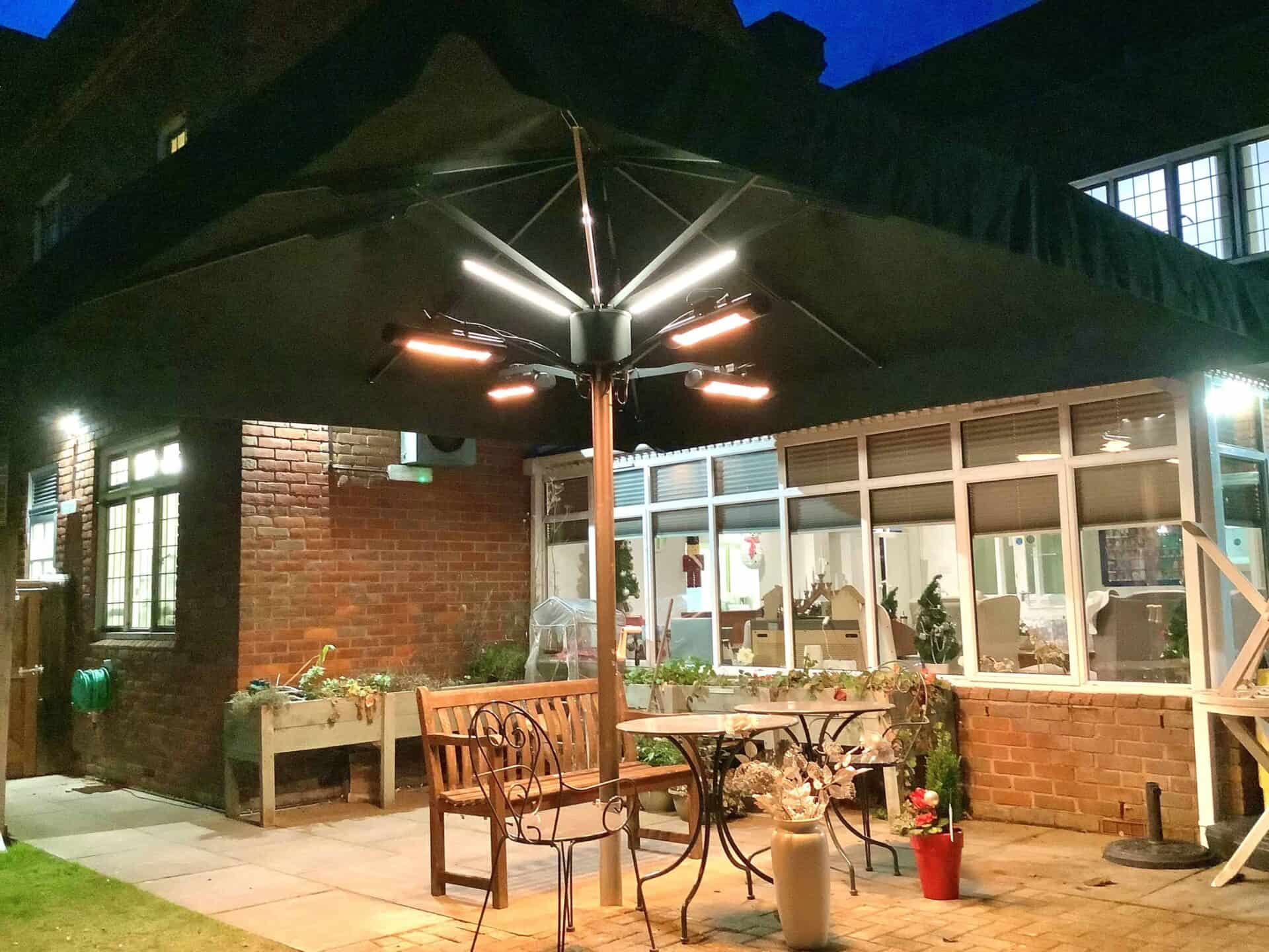 A cozy outdoor patio at dusk with warm lighting from an overhead fixture, featuring a metal table and chairs set, potted plants from a recent garden project, and a view into a brightly lit interior space