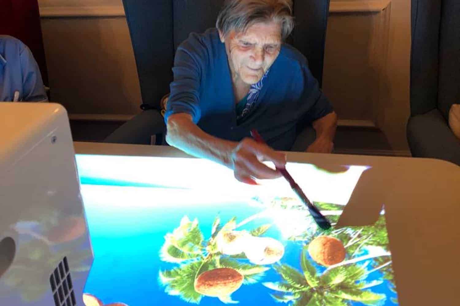 Elderly person engaging with technology, interacting with an Omi Interactive Board display featuring tropical imagery.