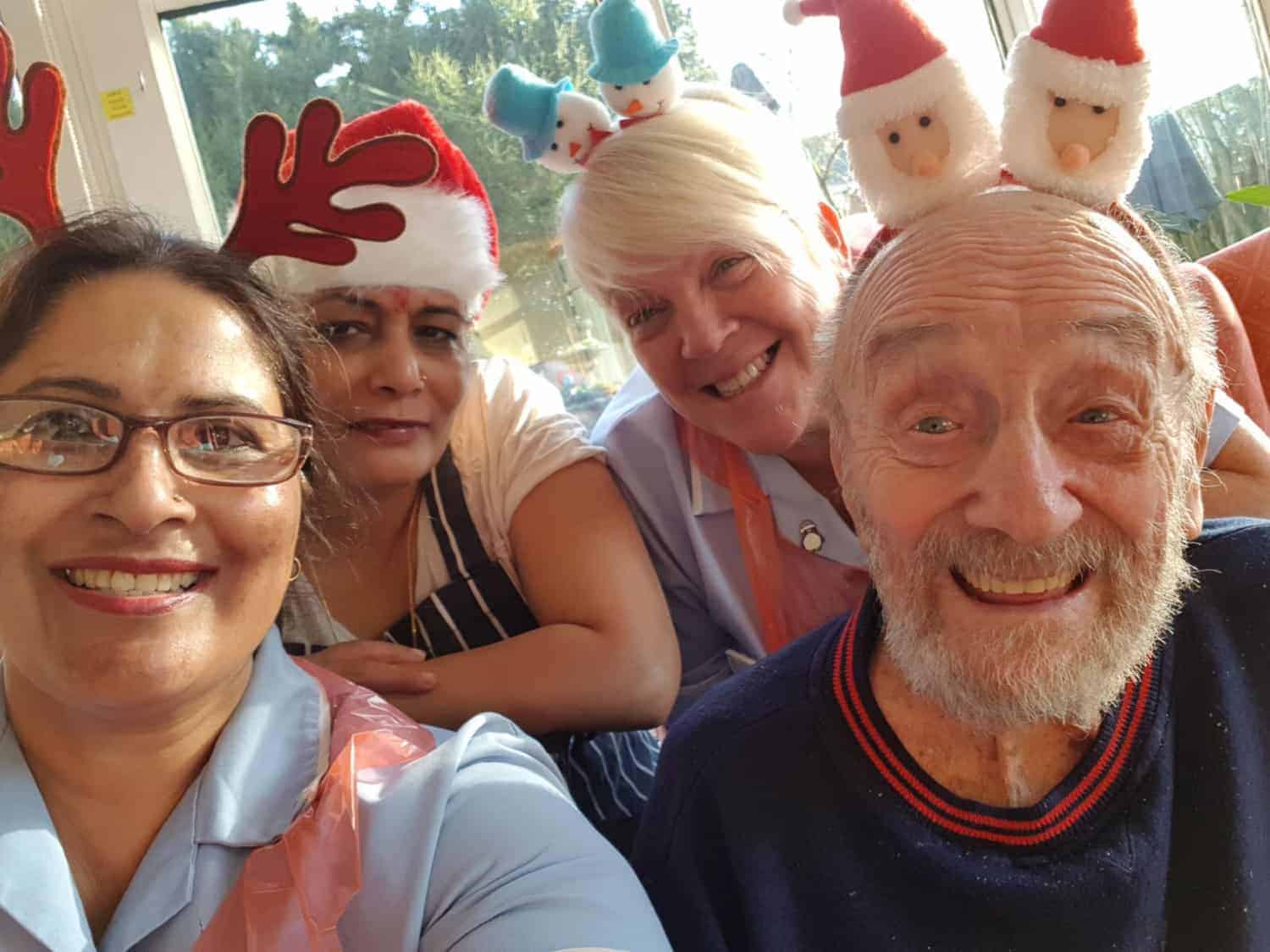 A cheerful group of people wearing festive holiday hats with Santa and reindeer designs, sharing a joyful moment together.