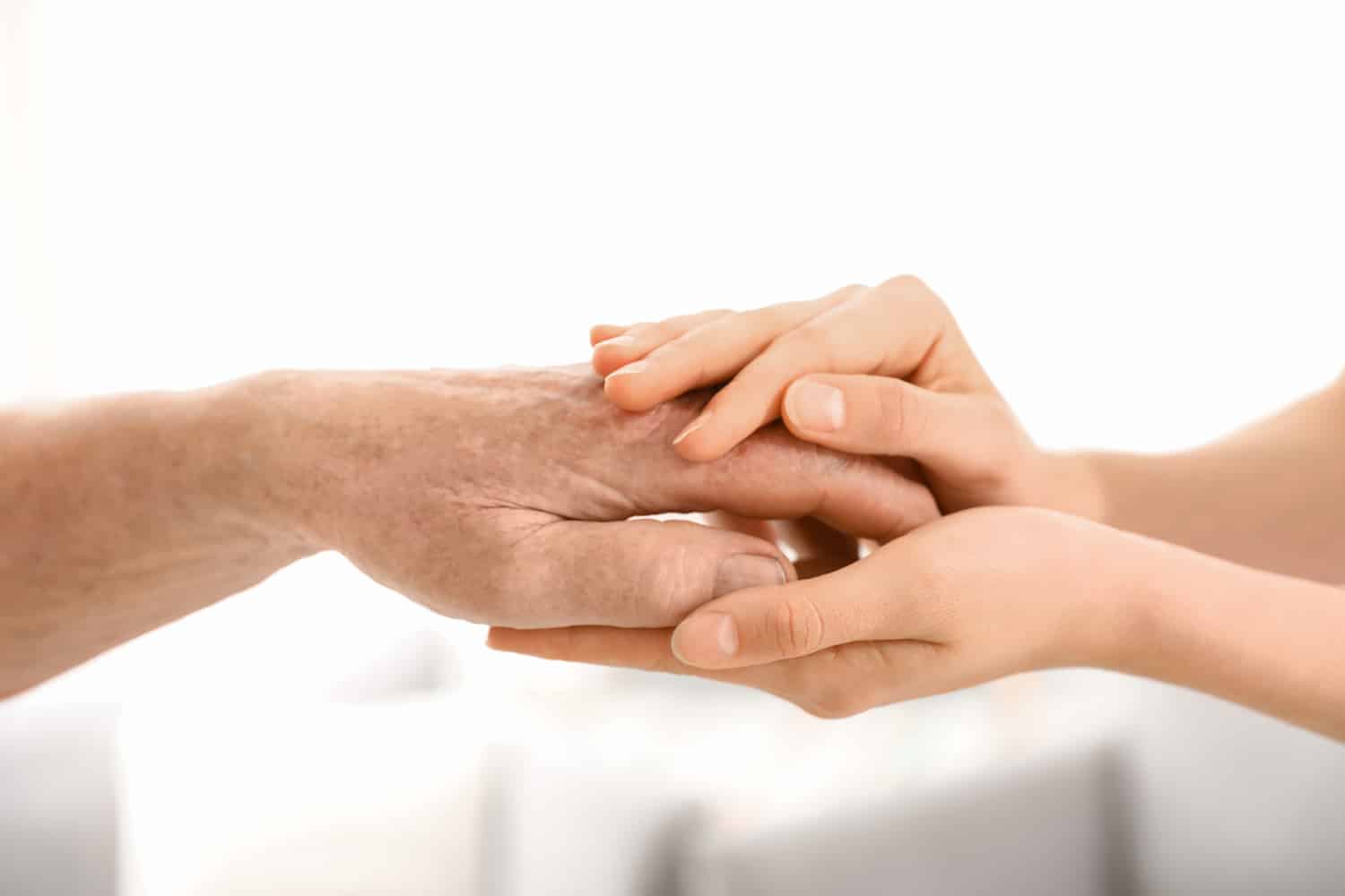 Two hands clasped in a caring and supportive gesture, symbolizing assistance, comfort, or compassion between generations in a nursing home.