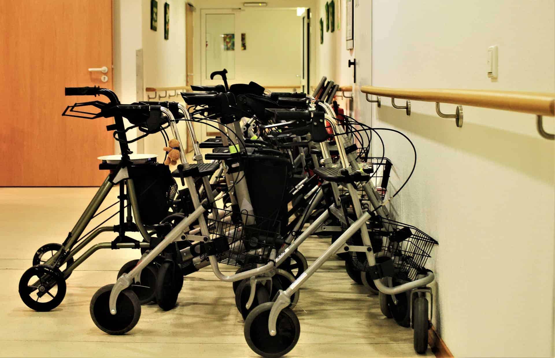 A collection of walking aids parked along a hallway, hinting at the presence of a rehabilitation center or elderly care facility following a reluctant parent's nursing home admission.