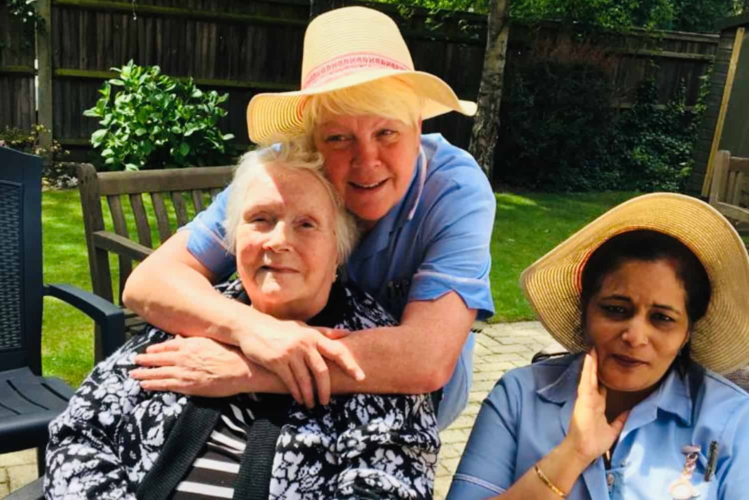 Three residents enjoying a sunny day outdoors, with two of them wearing stylish sun hats and all sharing a warm, cheerful moment together.