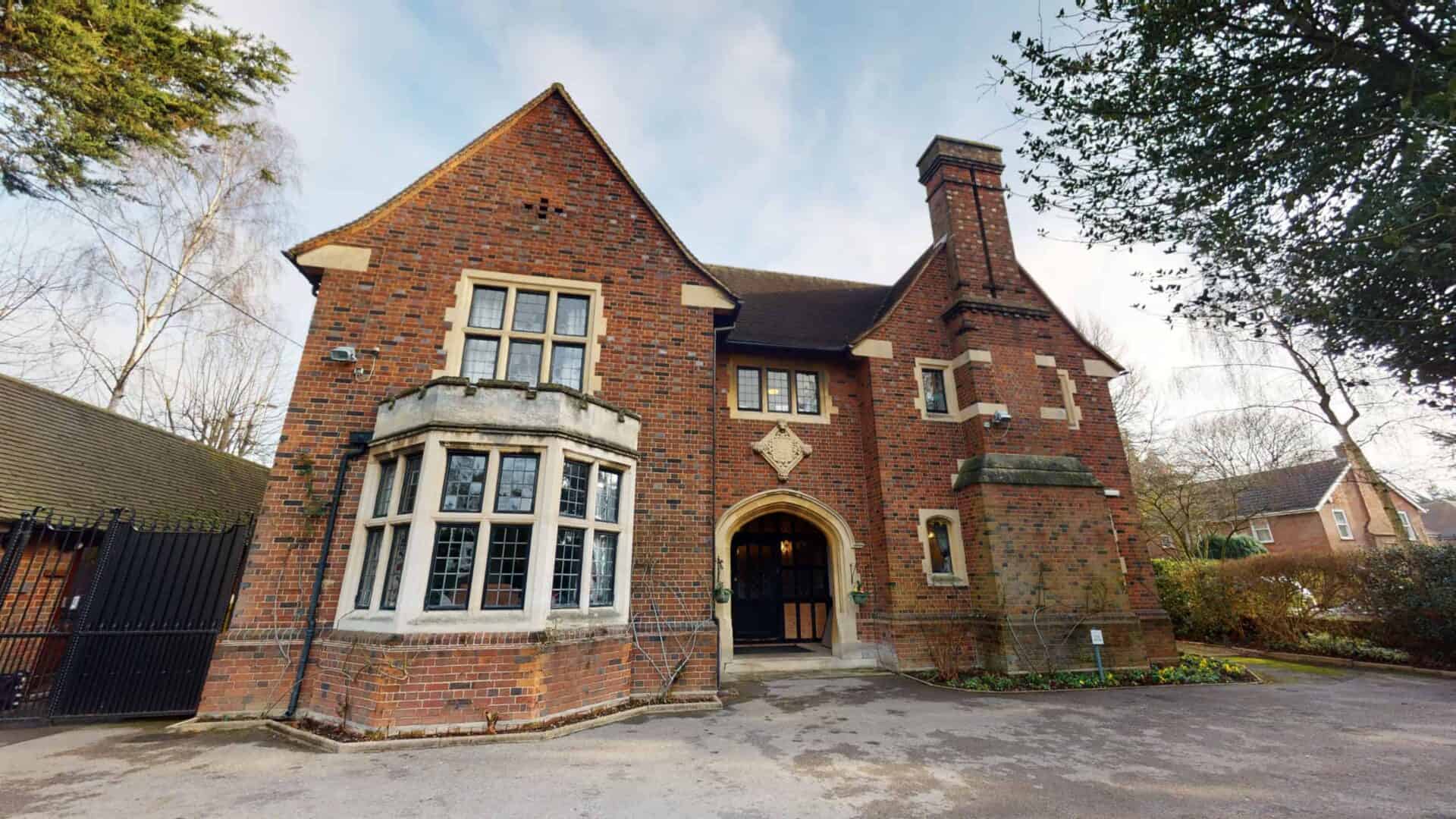 Charming brick tudor-style residential care home with a bay window and arched doorway nestled in a tranquil neighborhood.